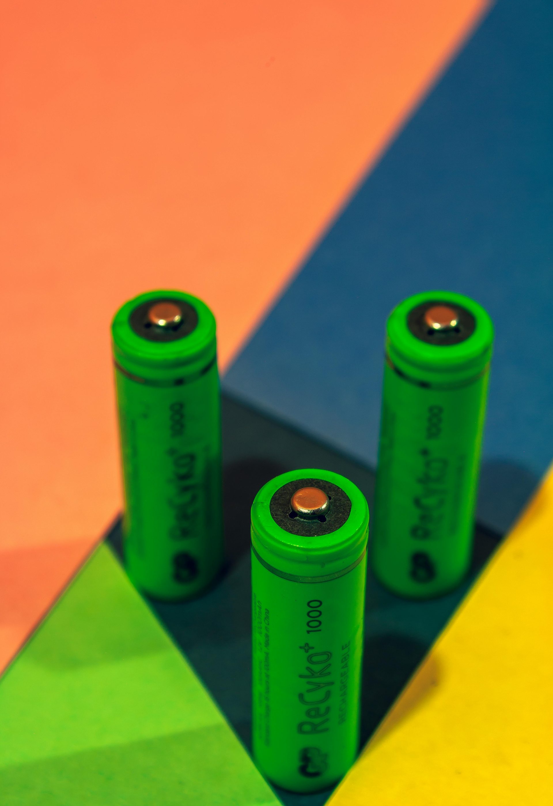 Three vibrant green batteries arranged on a colorful geometric background, showcasing modern electronics.